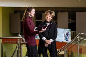 Woman in leadership role smiling and talking to another woman as they look at a booklet.