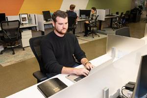 Man sitting at a cubicle typing on a laptop.