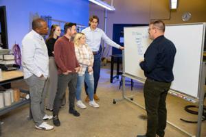 Instructor standing at whiteboard talking to group of adult class participants.